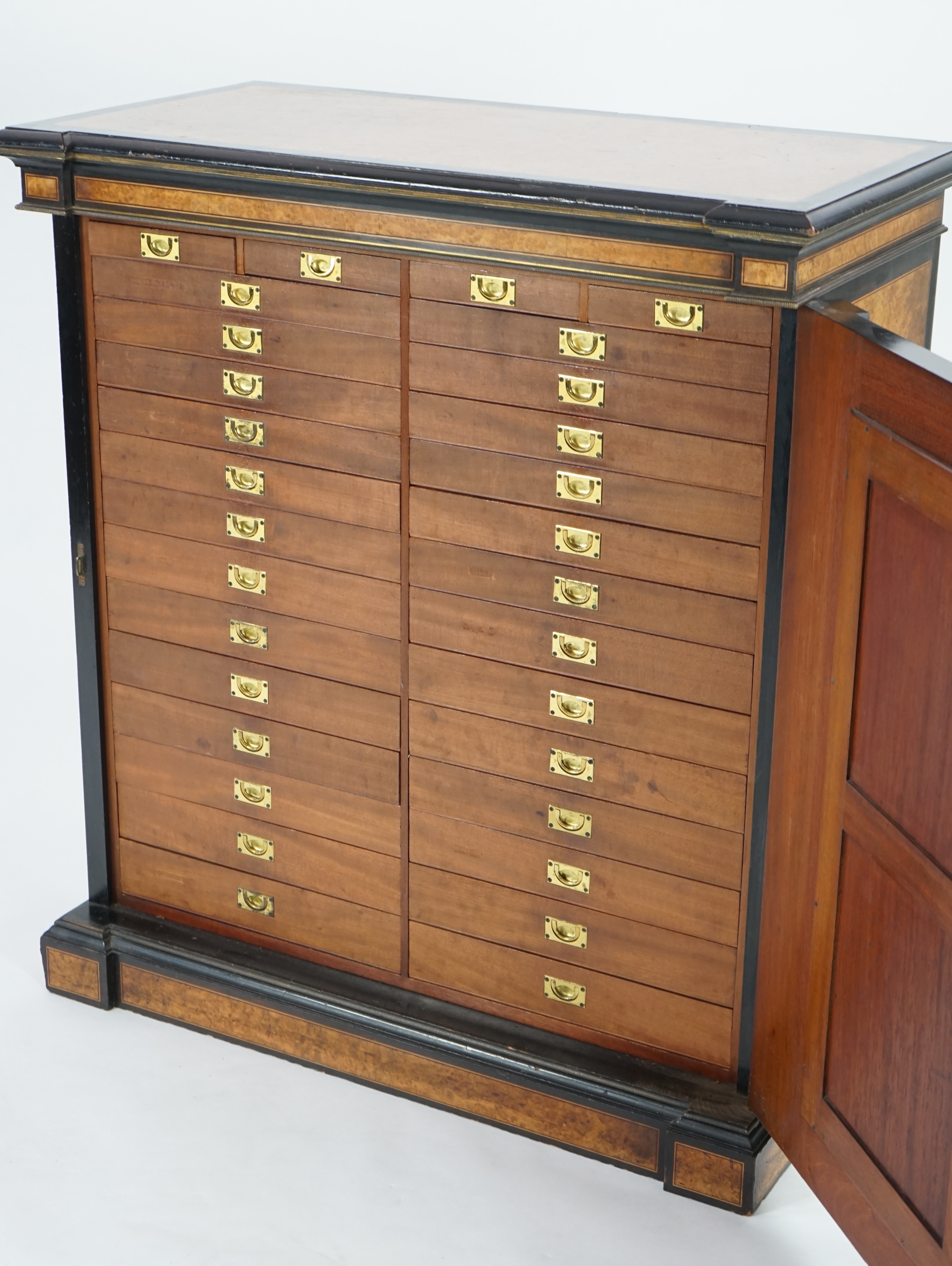 A Victorian ebony banded amboyna wood collector's cabinet, by Holland & Sons, with inverted breakfront top and single mirrored door enclosing four frieze and two banks of thirteen graduated drawers fitted with recessed b